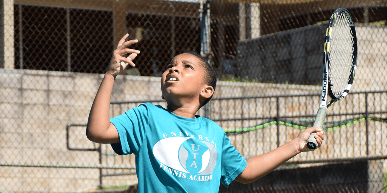 UTA (Universal Tennis Academy) McGhee Junior Program Boy Blue Shirt Serving